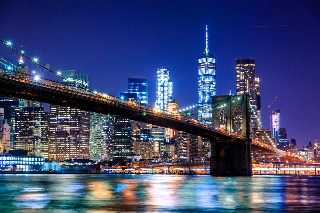 Brooklyn Bridge at night with illuminated Manhattan skyline and One World Trade Center in New York City.