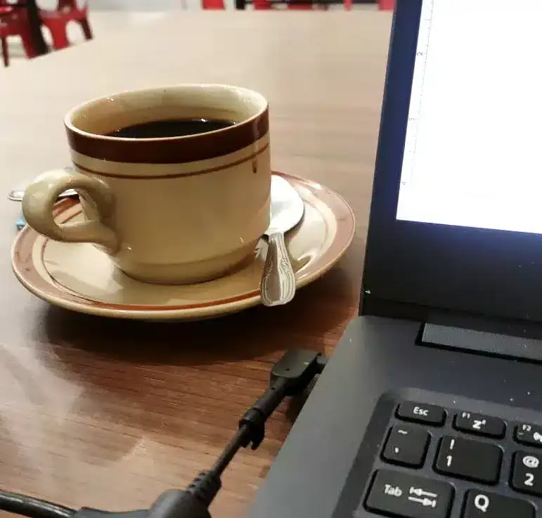 A cup of black coffee on a saucer beside a laptop on a wooden table, capturing a calm moment of reflection and creative thinking.
