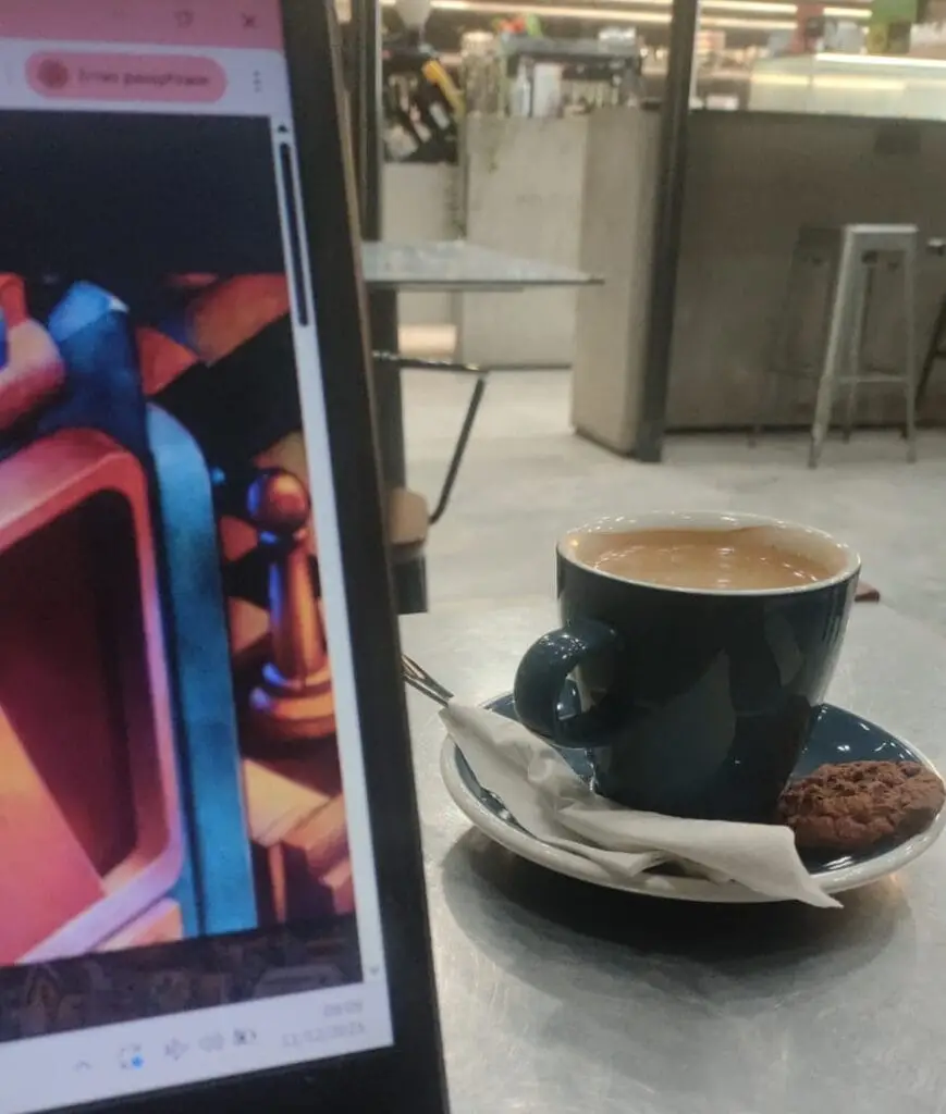 A cup of coffee beside a laptop in a quiet café, captured during a morning writing session reflecting on Schopenhauer’s view of suffering and the human will.
