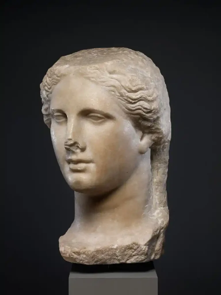 Hellenistic marble portrait bust of a Ptolemaic queen with wavy styled hair and subtle facial features on a dark background.